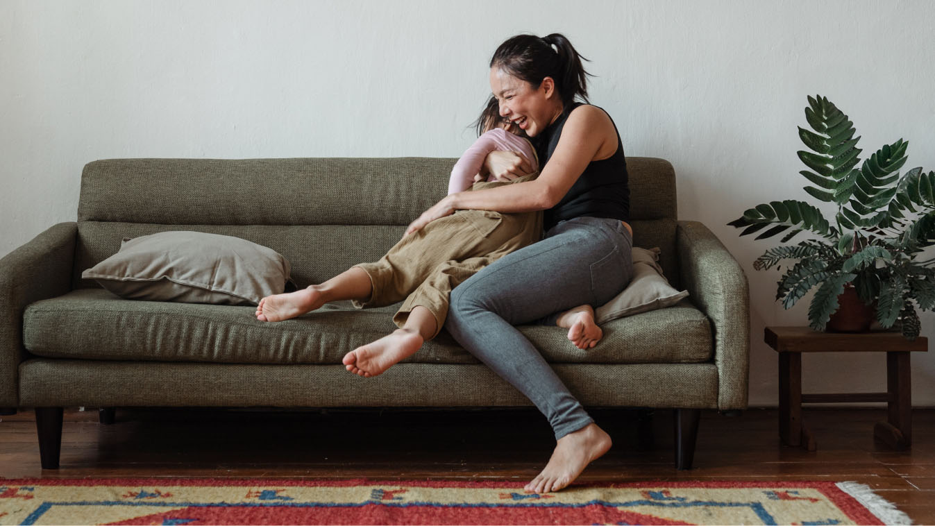 Mom hugging daughter on couch, laughing